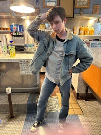 a young man in a denim jacket standing in a restaurant