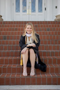 a woman in a graduation gown sitting on steps