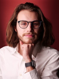 a man with long hair and glasses posing in front of a red background